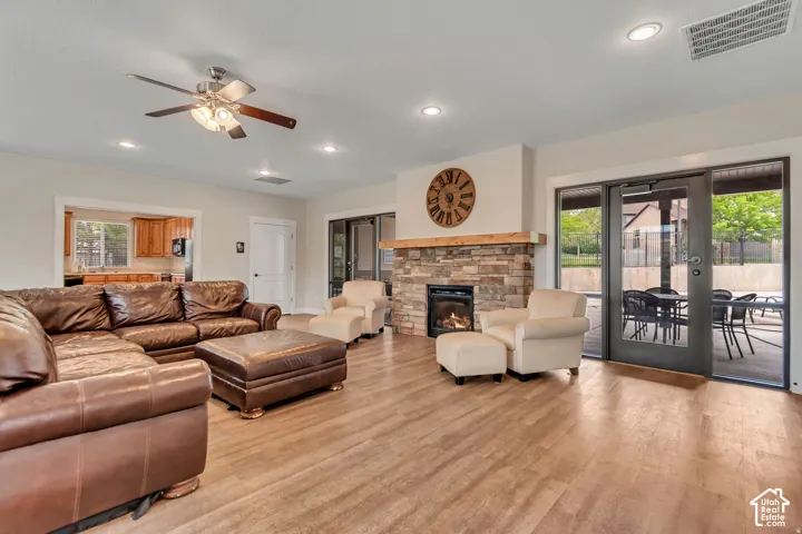Wood-finish flooring, stone-clad fireplace with wood mantle, recessed lighting, and ceiling fan