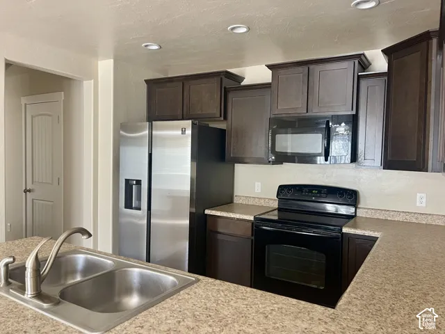Stainless steel refrigerator, black range, black over-the-range microwave, dark wood-finish cabinetry, and recessed lighting