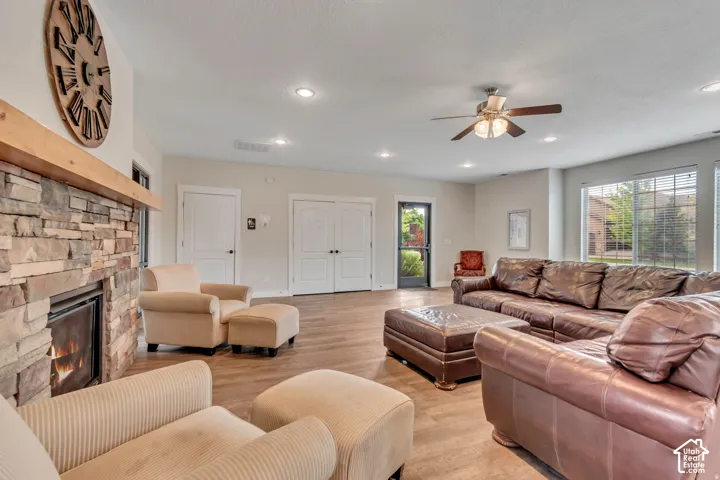 Spacious living area featuring a stone-clad fireplace with a wood mantel, wood-finish flooring, recessed lighting, a ceiling fan, and large windows
