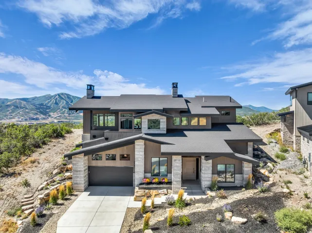 Contemporary architecture featuring a multi-level design, a gray asphalt shingle roof, stone and wood-panel exterior, an attached garage, and a concrete driveway