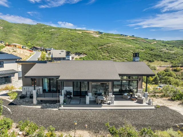 Modern architectural design with a dark shingle roof, extensive outdoor decking, large glass panels, and stone accents