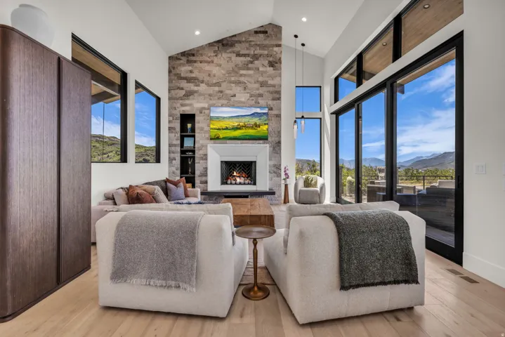 Vaulted ceilings with recessed lighting, stone-accented fireplace, wood-finish flooring, built-in shelving, and floor-to-ceiling windows