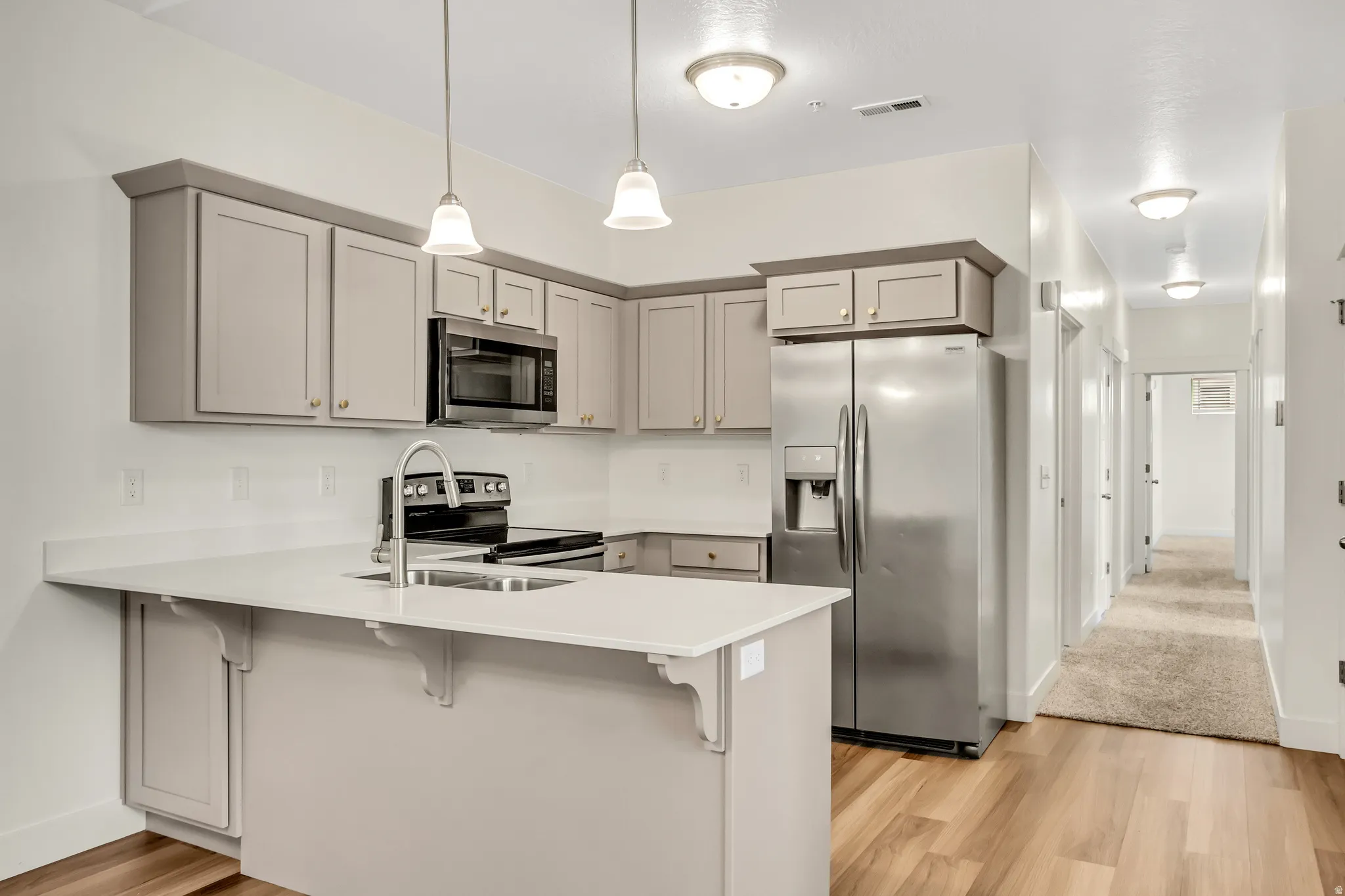 Kitchen featuring warm wood-finish flooring, light gray cabinetry, stainless steel appliances, and a white countertop island with a built-in sink