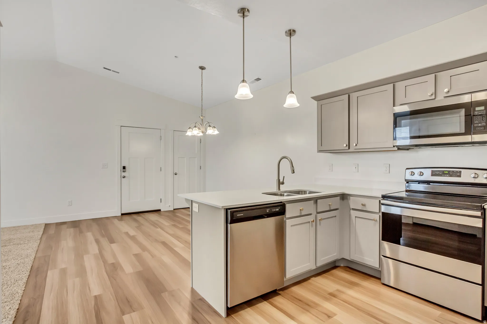Kitchen featuring light gray cabinetry, stainless steel appliances, white countertops, and wood-finish flooring