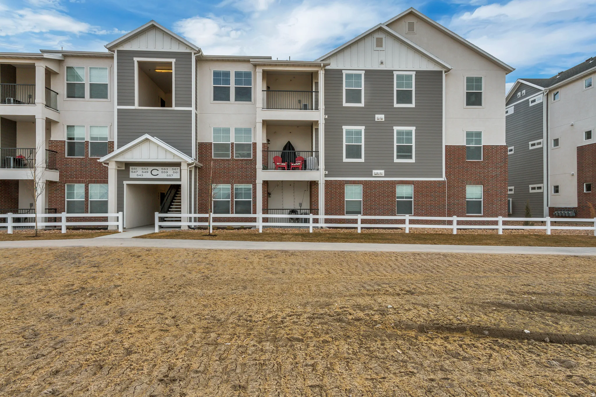 Multi-story property featuring brick and siding exterior, multiple private balconies, and a white fence bordering the foreground