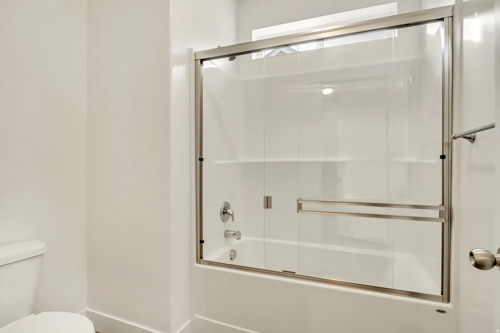 Bathtub with sliding glass enclosure, chrome fixtures, and integrated shelving