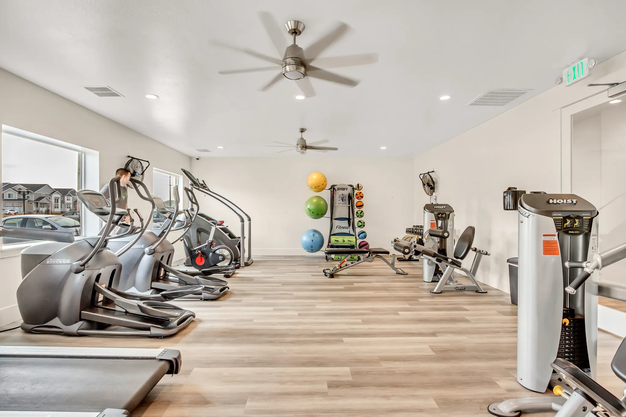 Fitness area featuring wood-finish flooring, two ceiling fans with integrated lighting, recessed lighting, and a large window
