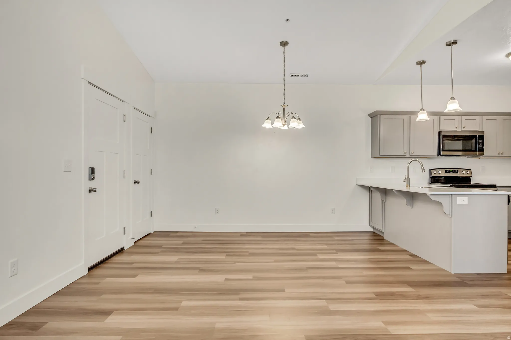 Open-concept living space with wood-finish flooring, white walls, and a contemporary chandelier