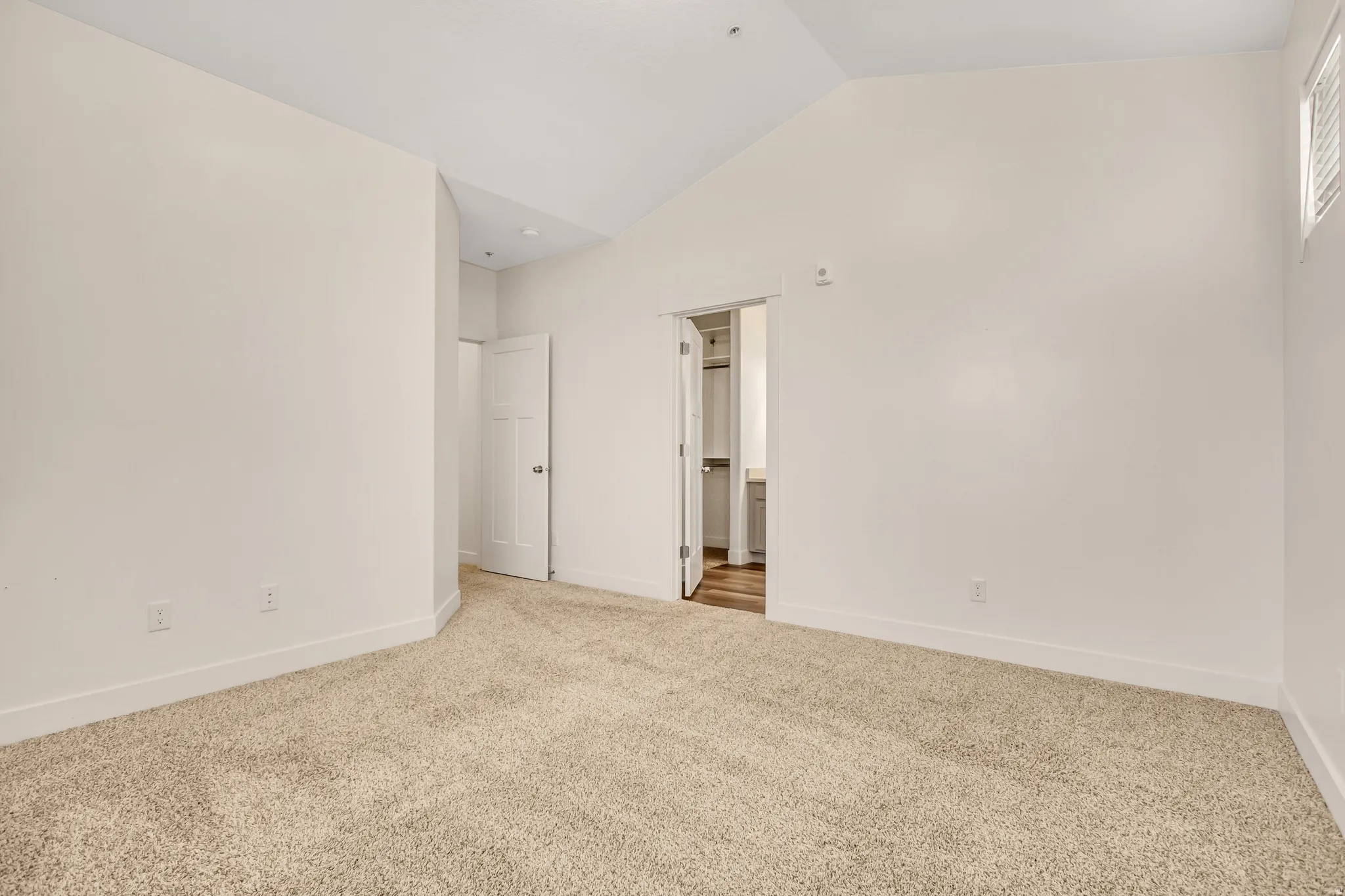 Vaulted ceiling, neutral wall finish, carpet flooring, window with louvered blinds, and a paneled door