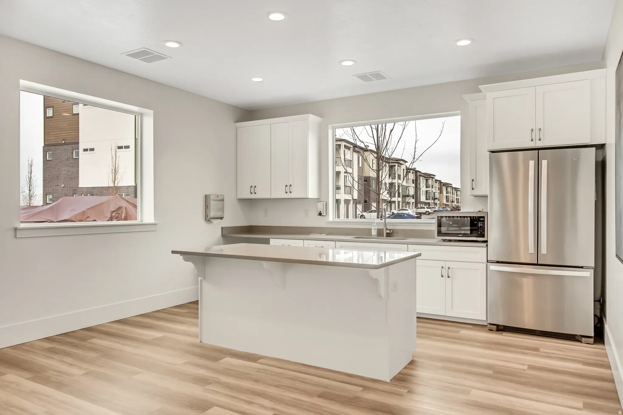 Kitchen featuring wood-finish flooring, white cabinetry, stainless steel refrigerator, recessed lighting, and a kitchen island with countertop space