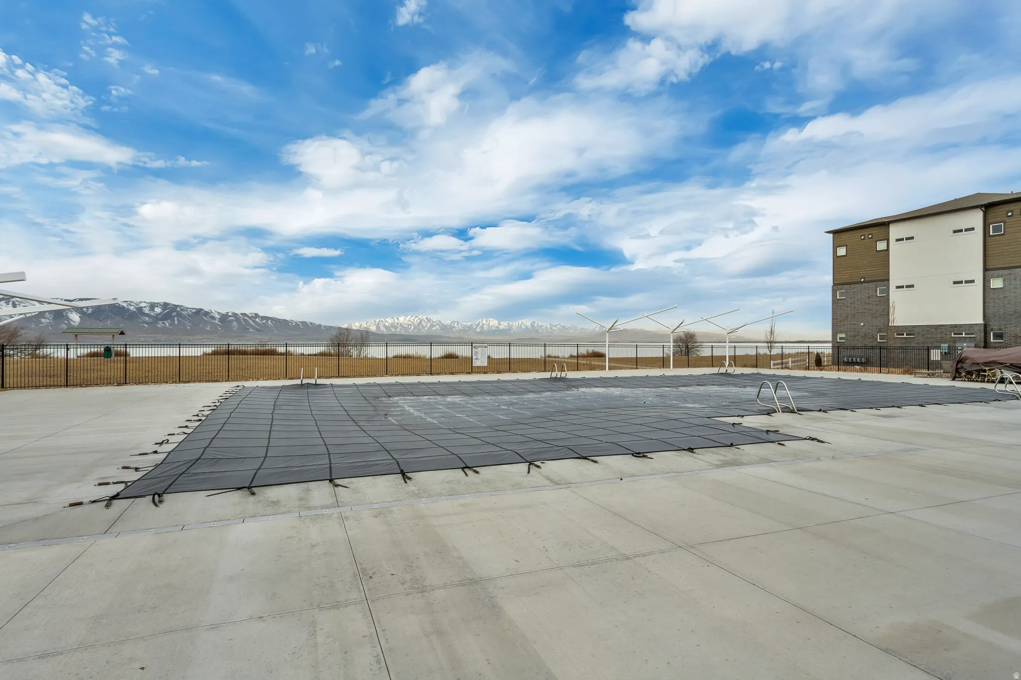Expansive concrete pool deck with a covered swimming pool and wrought iron fencing