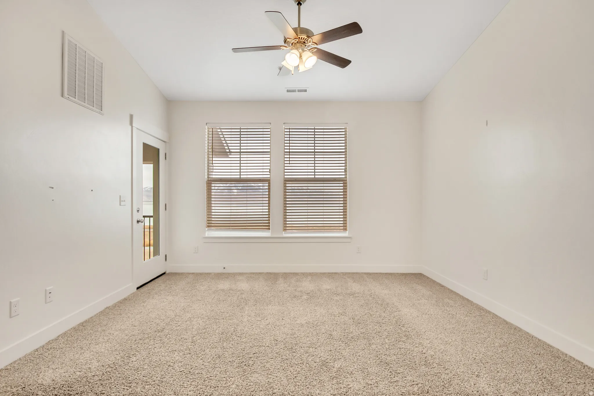 Neutral-toned carpet flooring, two windows with blinds, a glass-paneled door, and a ceiling fan with integrated lighting