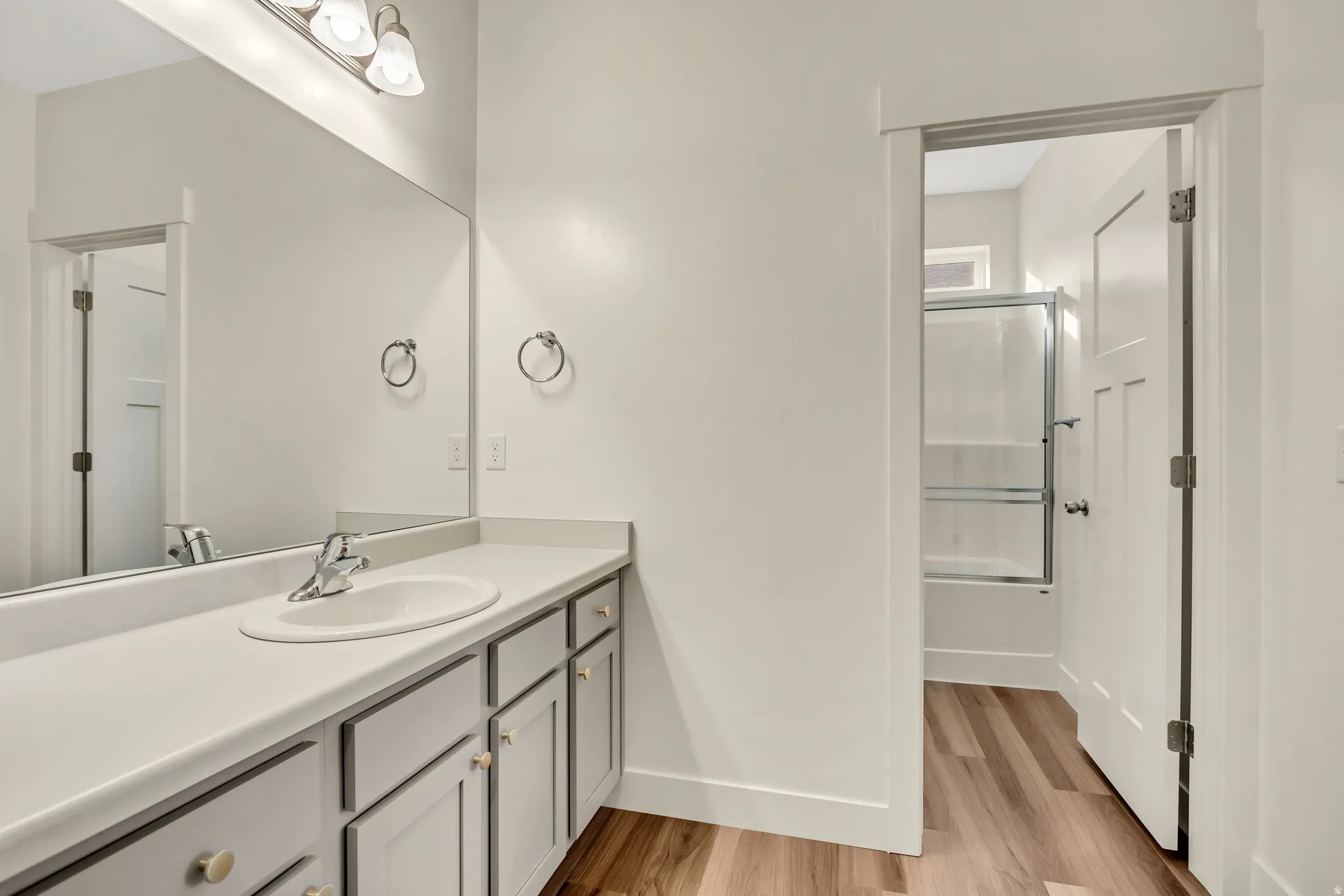 Vanity with an integrated sink, polished chrome faucet, expansive mirror, and wood-finish flooring