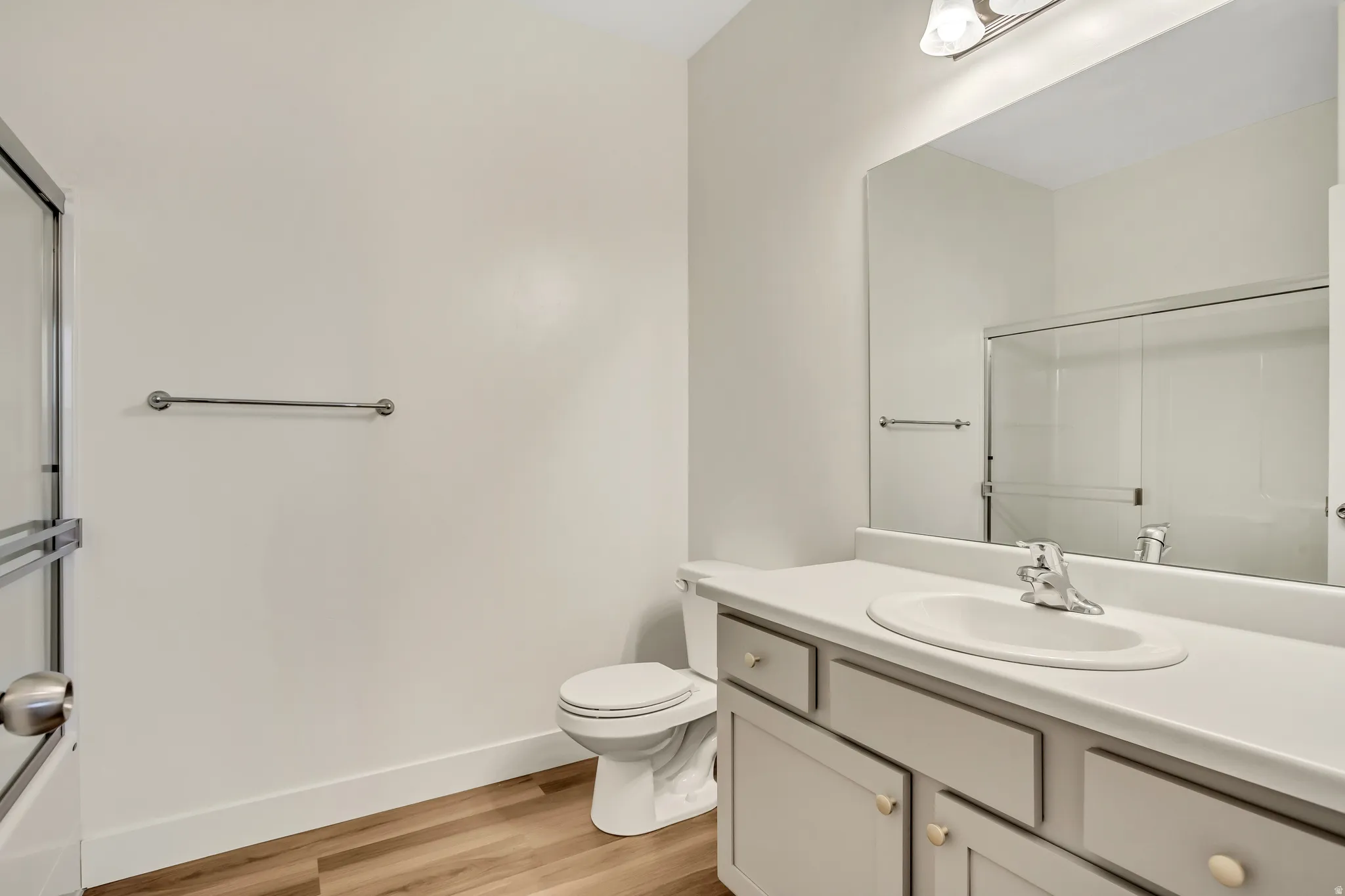 Bathroom featuring a single vanity with an integrated sink, large mirror, wood-finish flooring, and a glass-enclosed shower