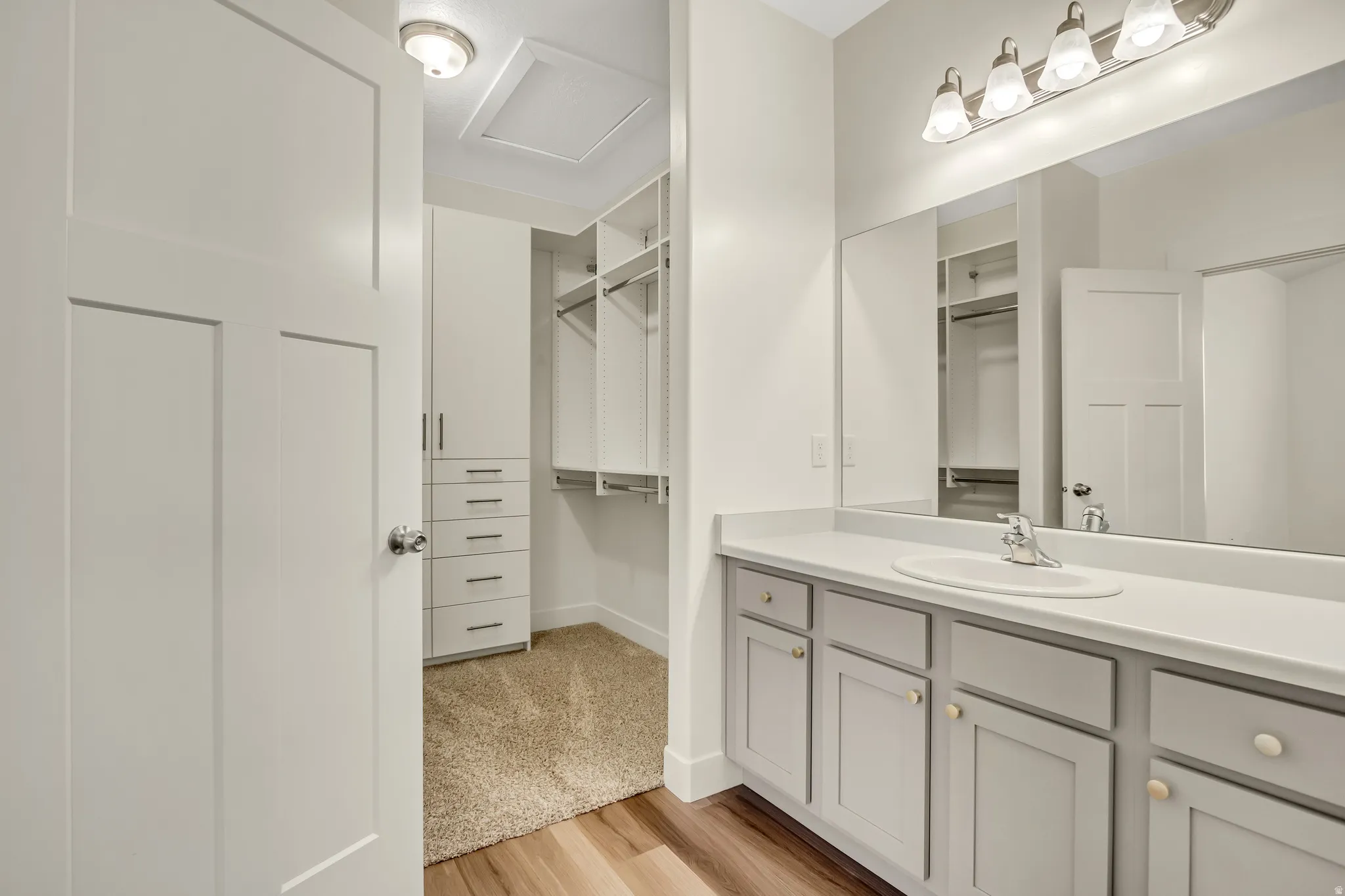 Vanity with an integrated sink and large mirror, gray-painted cabinetry with brass-toned hardware, and wood-finish flooring