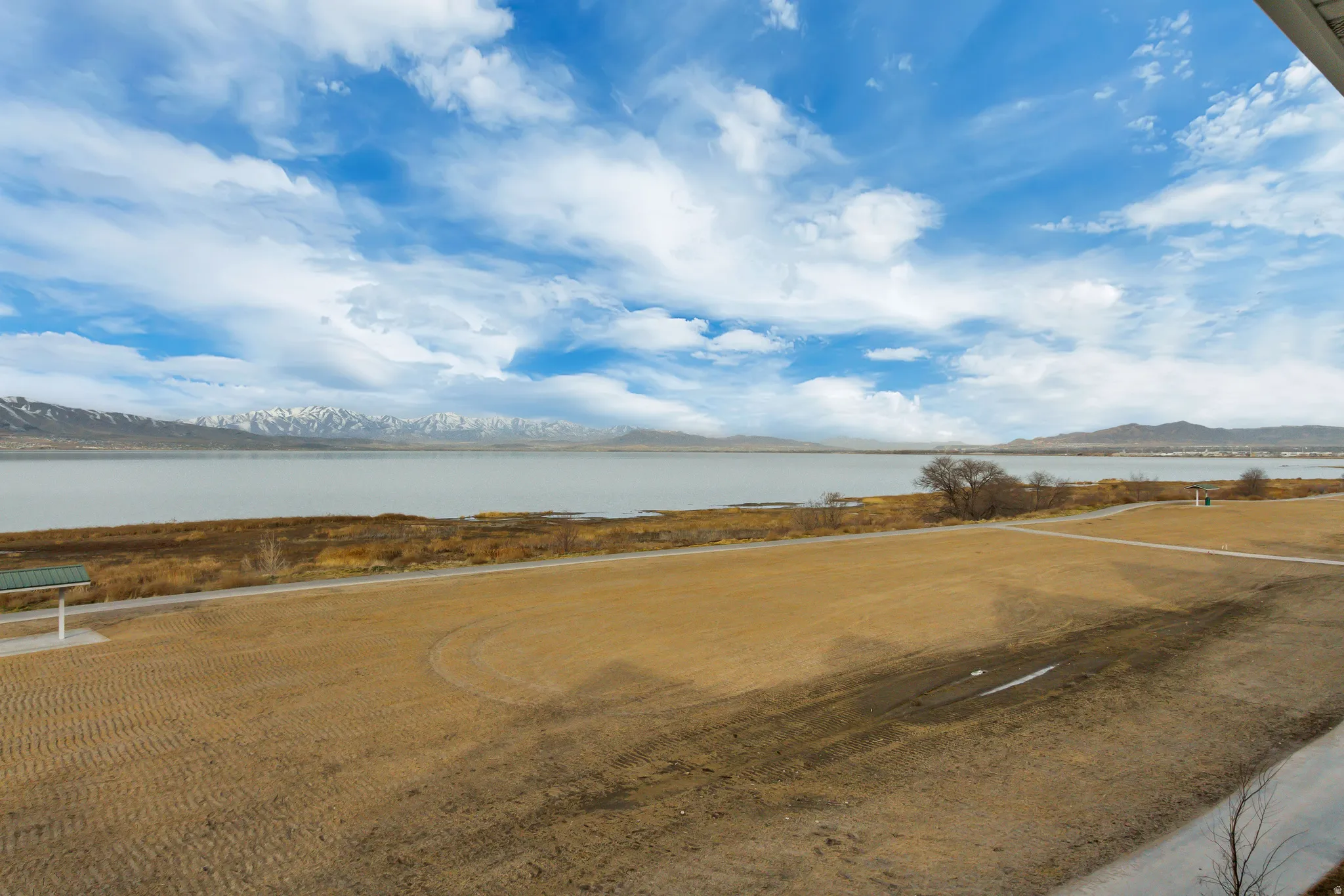Expansive outdoor area featuring a body of water, distant snow-capped mountains, and a paved walking path