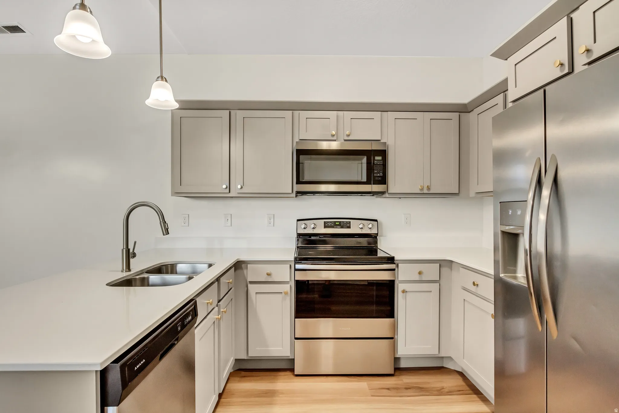 Modern kitchen with light gray cabinetry, stainless steel appliances, white countertops, and wood-finish flooring