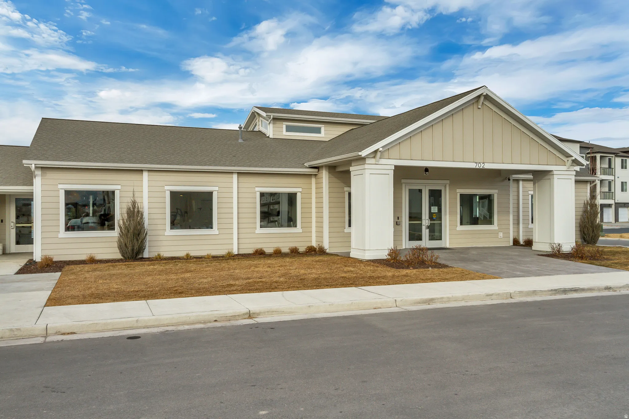 Contemporary exterior featuring light-toned siding, a covered entrance with substantial pillars, a gabled roofline, and multiple large windows