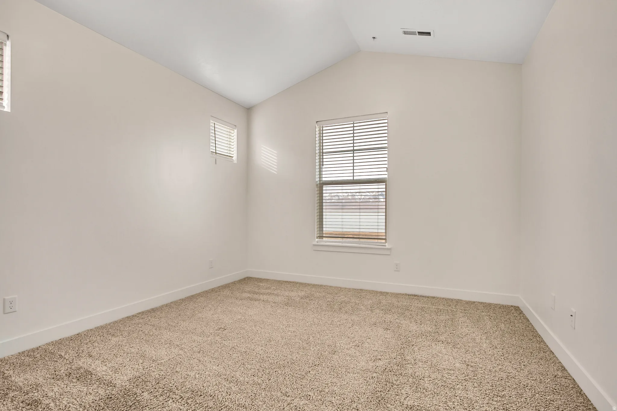 Vaulted ceiling, two windows with blinds, light-toned carpeting, and white walls