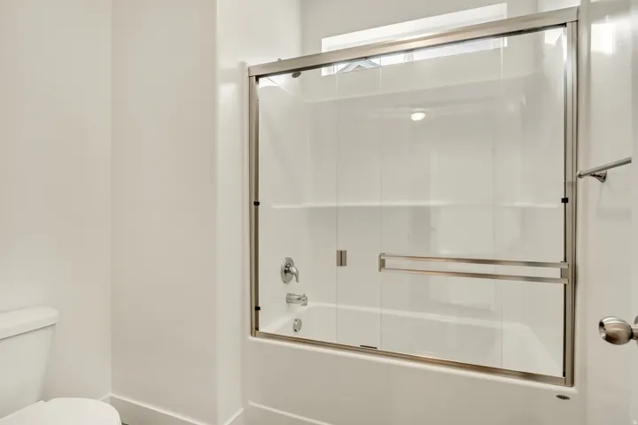 Bathtub with sliding glass enclosure, chrome fixtures, and integrated shelving