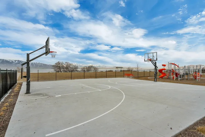 Outdoor concrete basketball court with two hoops, adjacent playground with slides and climbing structures, and a perimeter fence