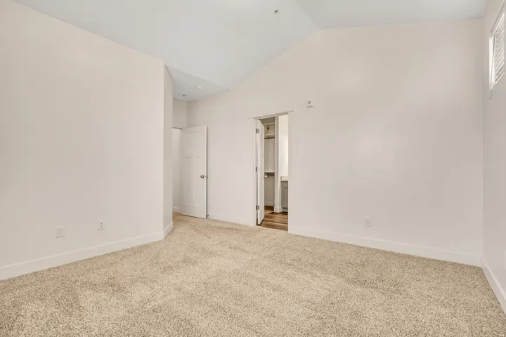 Vaulted ceiling, neutral wall finish, carpet flooring, window with louvered blinds, and a paneled door