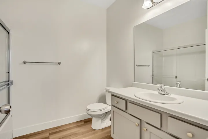 Bathroom featuring a single vanity with an integrated sink, large mirror, wood-finish flooring, and a glass-enclosed shower