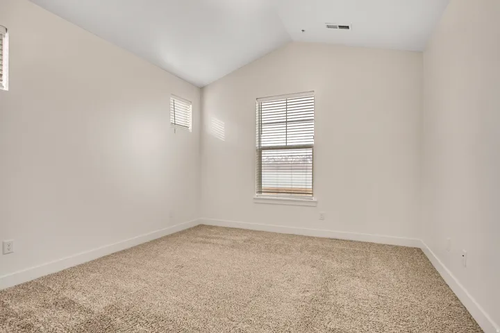 Vaulted ceiling, two windows with blinds, light-toned carpeting, and white walls