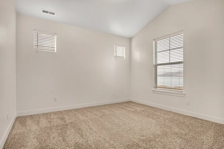 Vaulted ceiling, two windows with blinds, light-colored carpet, and white walls