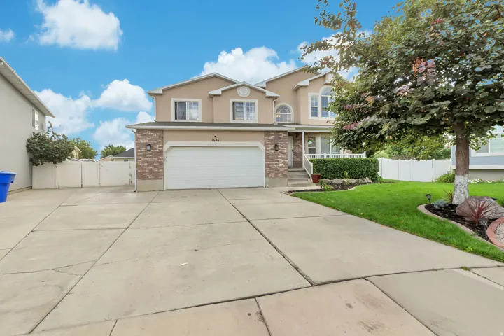 Two-story stucco and brick exterior, two-car garage, concrete driveway, front lawn with landscaping, and white fencing