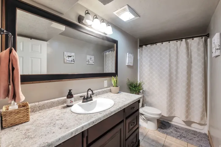 Vanity with a large mirror, a single basin sink, a dark wood-finish cabinet, and a light-toned countertop