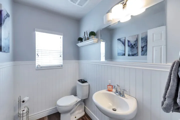 Wall-mounted pedestal sink with chrome faucet, wood-finish flooring, and white wainscoting