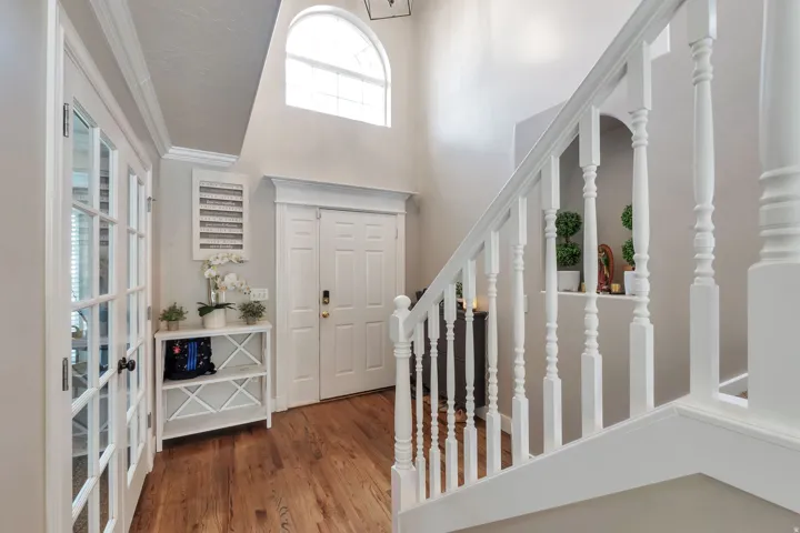 Double front entry doors, wood-finish flooring, white banister with turned balusters, arched transom window, and white French doors