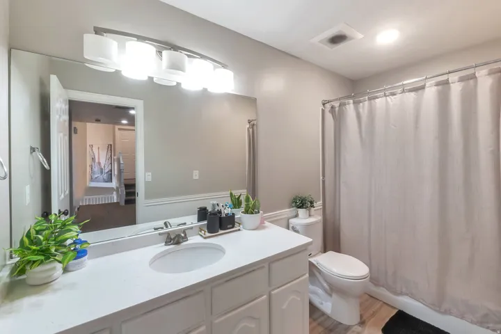 Vanity with an integrated sink, broad wall mirror, overhead lighting fixture, and a toilet