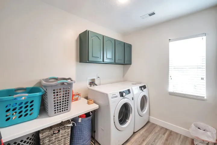 Upper cabinetry, a window with blinds, and wood-finish flooring