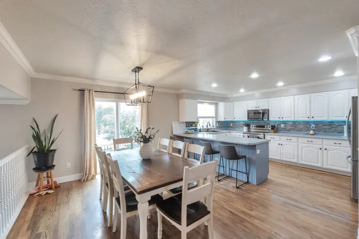Kitchen and dining area featuring wood-finish flooring, white cabinetry, a kitchen island with seating, a glass tile backsplash, and stainless steel appliances