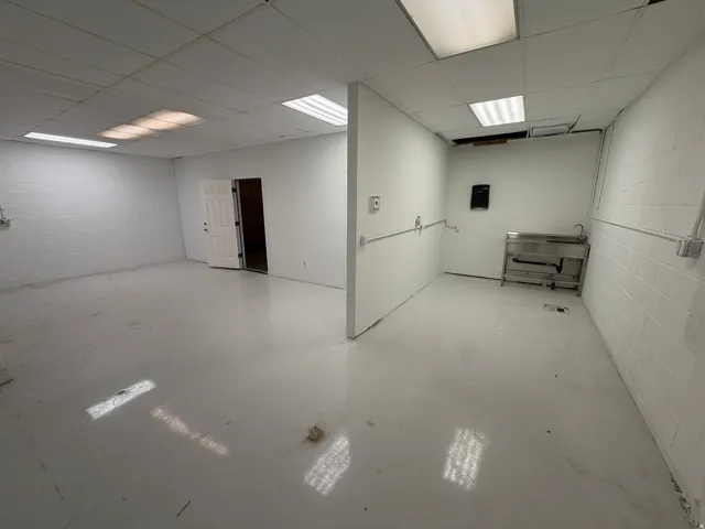 Spacious room with white walls, drop ceiling, fluorescent lighting, and a stainless steel utility sink