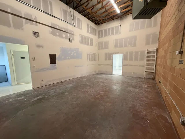 Exposed wood ceiling beams, high ceilings, brick wall construction, concrete flooring, and an open layout