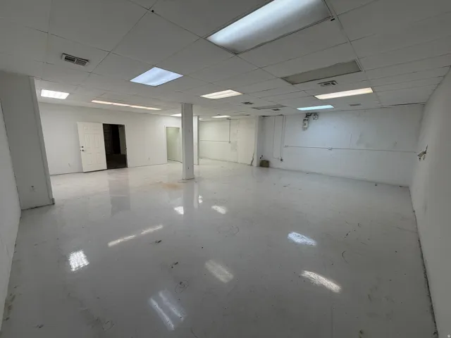 Expansive open area with white walls, polished concrete flooring, and a grid ceiling with integrated fluorescent lighting