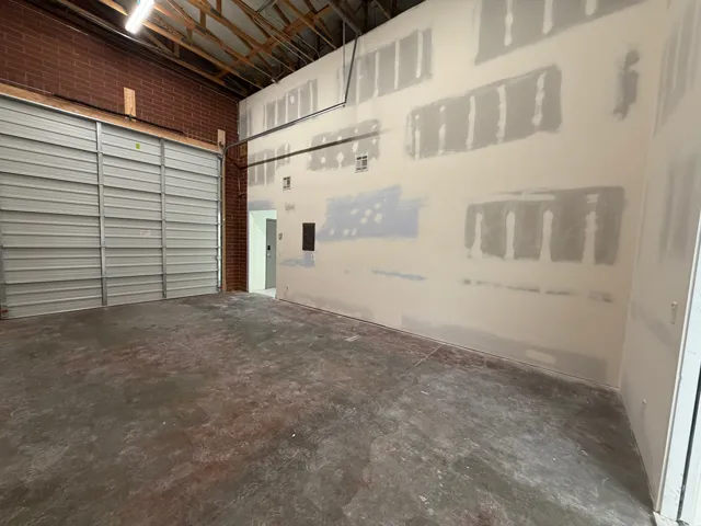 Exposed ceiling rafters, concrete flooring, brick wall accent, roll-up door, interior access door