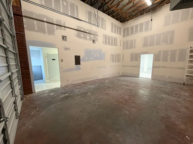 High ceilings with exposed wood beams, concrete flooring, roll-up garage door, exposed brick column, and multiple interior doorways