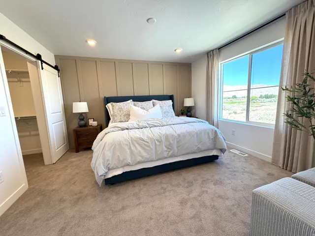Recessed ceiling lighting, full-height accent wall, wide window, soft carpeting, and a sliding barn door
