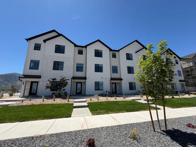 Modern townhouse exterior featuring white vertical siding, light gray stucco, a contrasting dark roofline, and multiple dark-framed windows