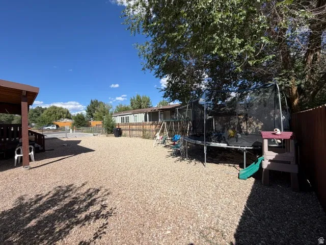 Expansive gravel yard featuring a wood privacy fence, mature trees, and a covered patio structure