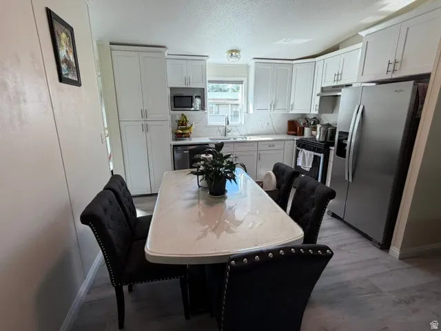 White upper and lower cabinetry, stainless steel appliances, wood-finish flooring, and a white countertop