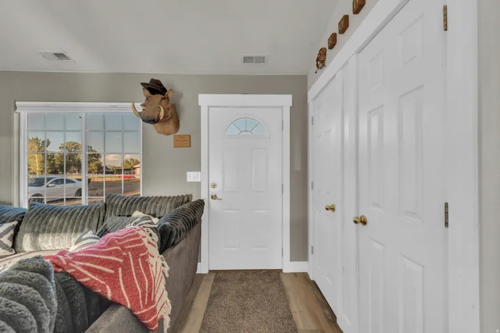 Bright entryway with multi-panel white entry door featuring transom window detail, extensive closet storage with dual brass hardware, and wood-finish flooring throughout