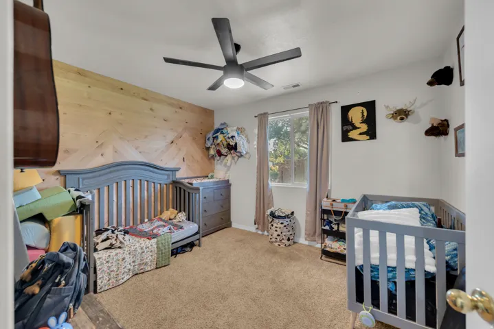 Accent wall with wood paneling, ceiling fan with integrated lighting, window with curtain rods, wall-to-wall carpeting, white painted walls