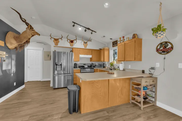 Kitchen featuring wood-finish flooring, vaulted ceiling, wood cabinetry, stainless steel appliances, and track lighting
