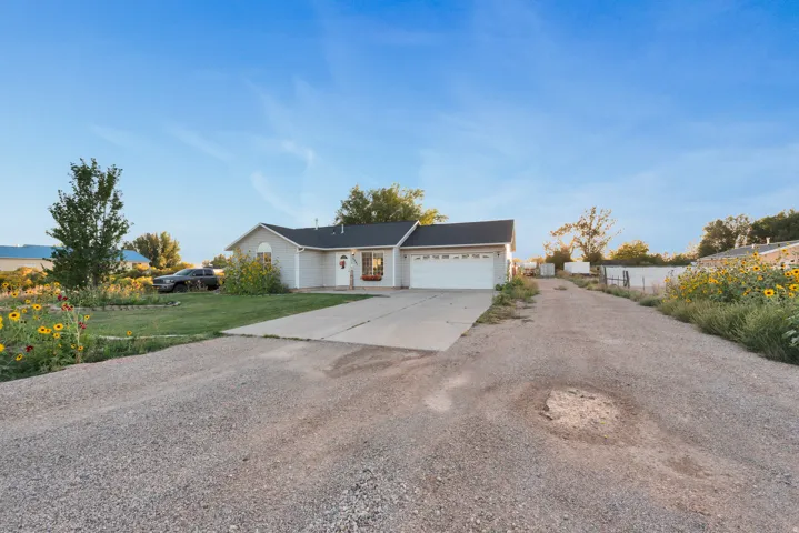 Light gray siding exterior with a dark roof, attached garage, concrete driveway, and a gravel pathway
