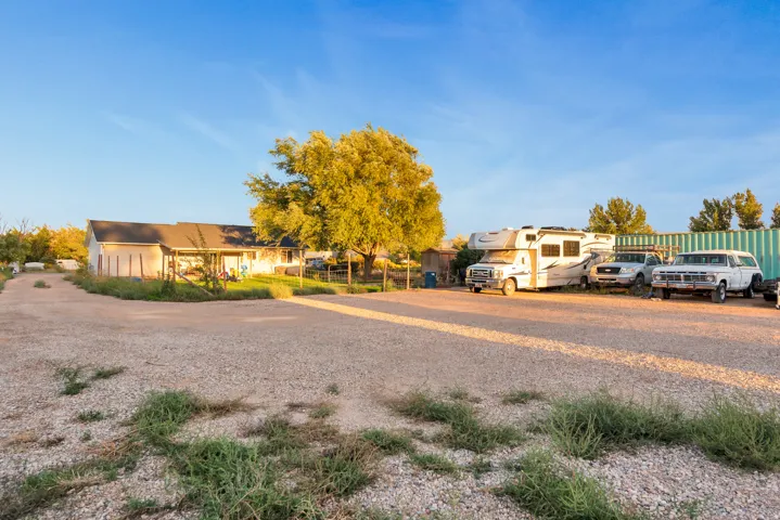 Gravel parking area with partial fencing and distant residential structure